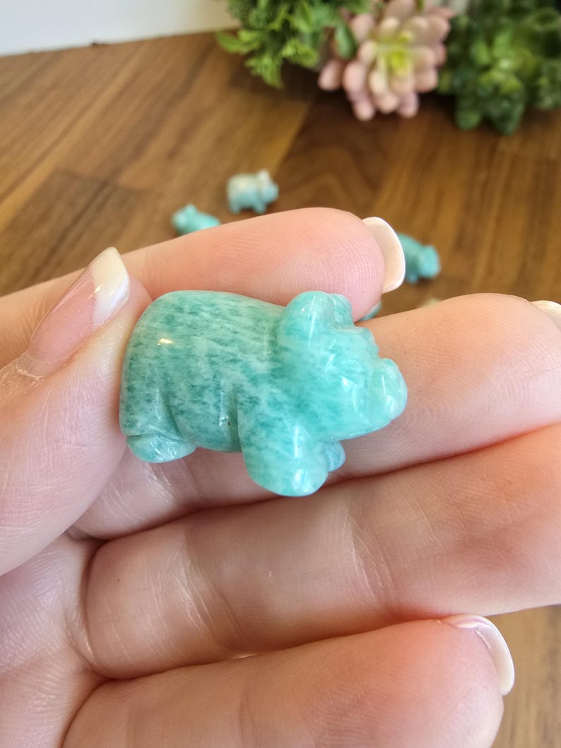 May include: A small, hand-carved figurine of a pig made from polished amazonite stone. The stone features a mottled, opaque teal and light green color palette with natural white veining throughout the smooth, rounded surface of the animal sculpture.