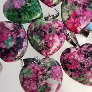 May include: Heart-shaped pendants made of ruby zoisite stone. The pendants feature a mix of pink, green, and black colors. Each pendant has a silver-colored bail attached at the top for hanging.