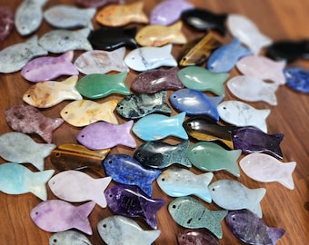 May include: A collection of small, flat, fish-shaped carvings made from various polished gemstones in a wide array of colors including blue, green, purple, black, white, and brown, each featuring a small drilled hole near the head.