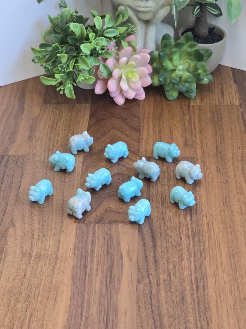 May include: A collection of twelve small, carved light blue stone figurines shaped like pigs. Each miniature animal figure features a smooth, polished surface with subtle variations in color and texture, arranged in a scattered formation.