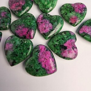 May include: A collection of ten heart-shaped green and pink gemstones. The stones are polished and have a smooth, glossy finish.