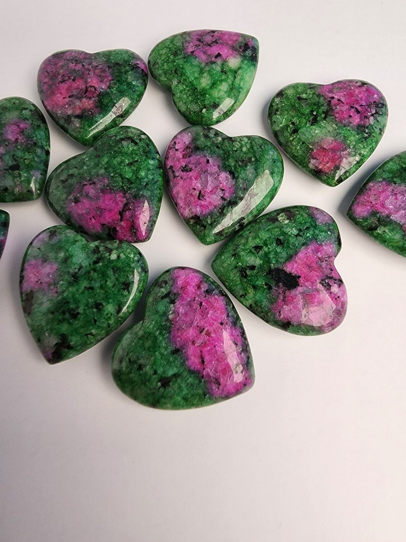 May include: A collection of ten heart-shaped green and pink gemstones. The stones are polished and have a smooth, glossy finish.