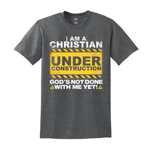 May include: A heather grey t-shirt with a yellow and black construction sign that reads "I am a Christian Under Construction God's not done with me yet!"