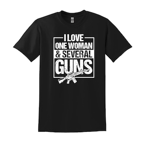 May include: Black t-shirt with the text "I LOVE ONE WOMAN & SEVERAL GUNS" in white block letters. A graphic of a rifle is below the text. The shirt is a short-sleeved crew neck.