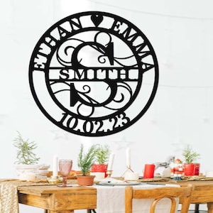 Könnte beinhalten: Schwarze Wanddekoration aus Metall mit den Namen Ethan und Emma, dem Nachnamen Smith und dem Datum 10.02.23. Die Namen sind in einem Kreis mit einem Herzsymbol dazwischen angeordnet. Der Nachname befindet sich auf einer separaten Zeile unter den Namen. Das Datum befindet sich unter dem Nachnamen.