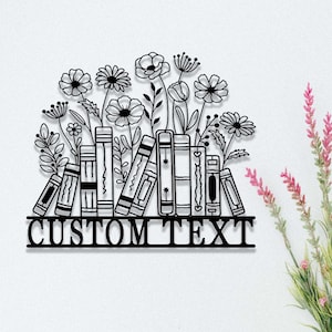 May include: Black metal wall decor featuring a stack of books with flowers growing out of the top. The text "CUSTOM TEXT" is displayed on a banner below the books.