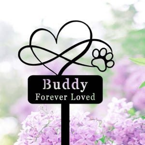 May include: Black metal garden stake with an infinity heart design and a paw print. The stake has a sign that reads "Buddy Forever Loved".
