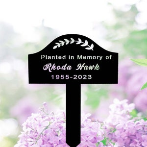 Könnte beinhalten: Schwarzer Gartenpflock aus Metall mit abgerundeter Oberseite und einem Blattdesign. Der Pflock trägt die Gravur "Planted in Memory of Rhoda Hawk 1955-2023".