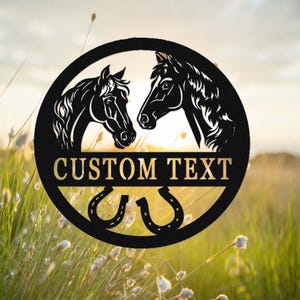 May include: Black metal silhouette of two horses' heads facing each other, with a horseshoe design below. The text "CUSTOM TEXT" is displayed in a gold banner.