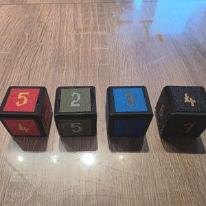 May include: Four black dice with different colored faces. The dice are numbered 2, 3, 4, and 5. The dice are on a wooden surface.