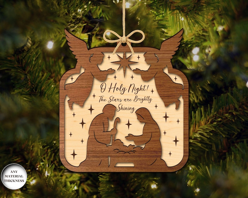 May include: Wooden Christmas ornament with a layered design. The ornament features a nativity scene with angels, stars, and the text "O Holy Night! The Stars are Brightly Shining". It is suspended by a natural twine.