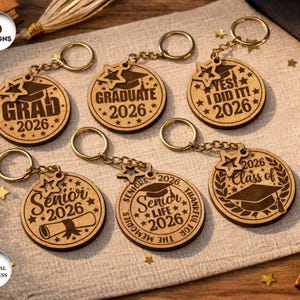 May include: A collection of six wooden graduation keychains. Each keychain features a round design with gold-colored hardware and engraved text such as "Grad 2026", "Graduate 2026", and "Senior 2026".