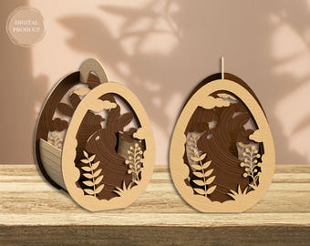 Könnte beinhalten: Zwei hölzerne Ostereier-Dekorationen mit filigranen Ausschnitten von einem Hasen, Blumen und Wolken. Die Dekorationen sind aus hellem braunem Holz gefertigt und haben eine natürliche Holzoptik.