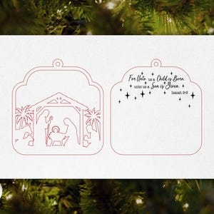 May include: A white Christmas ornament with a red outline of a nativity scene and the text "For Unto us a Child is Born, unto us a Son is Given, Isaiah 9:6". The ornament has a decorative shape with a hole for hanging.