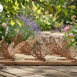 Puede incluir: Seis esculturas decorativas de metal con forma de libélula y diseños intrincados en las alas se exhiben sobre una superficie de madera. Las libélulas son de color marrón cálido y están sobre un fondo de jardín florido.