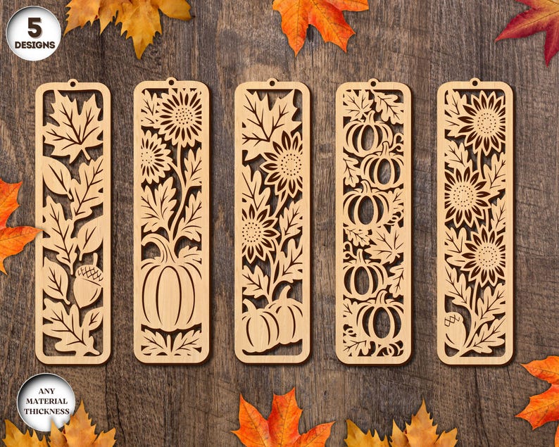 May include: Five wooden bookmarks with intricate cut-out designs. The designs include leaves, sunflowers, pumpkins, and acorns. The bookmarks are light brown and have a small hole at the top. The text "5 DESIGNS" and "ANY MATERIAL THICKNESS" are in the image.