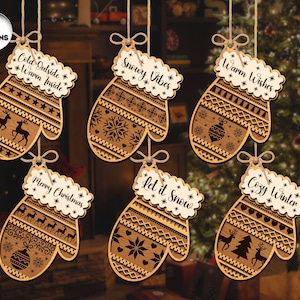 May include: Six wooden mitten ornaments with festive designs and text. Each ornament features a different design, including reindeer, snowflakes, and Christmas tree motifs. The text on the ornaments includes phrases like "Cold Outside, Warm Inside" and "Merry Christmas."