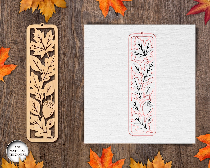 May include: A wooden bookmark with a leaf and acorn design. The bookmark is rectangular with a cutout pattern of leaves and an acorn. The bookmark is light brown and has a hole at the top for a tassel. The design is repeated in red on a white background.