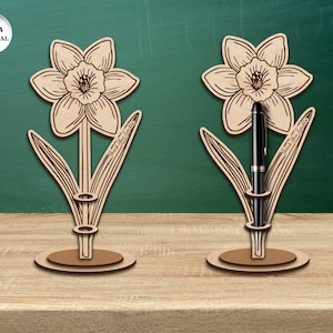 Pu&ograve; includere: Due portapenne in legno a forma di narciso, uno dei quali contiene una penna nera. I portapenne sono realizzati in materiale da 3 mm e riportano il testo "Grazie Insegnante".