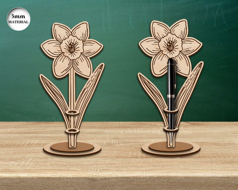 Pu&ograve; includere: Due portapenne in legno a forma di narciso, uno dei quali contiene una penna nera. I portapenne sono realizzati in materiale da 3 mm e riportano il testo "Grazie Insegnante".