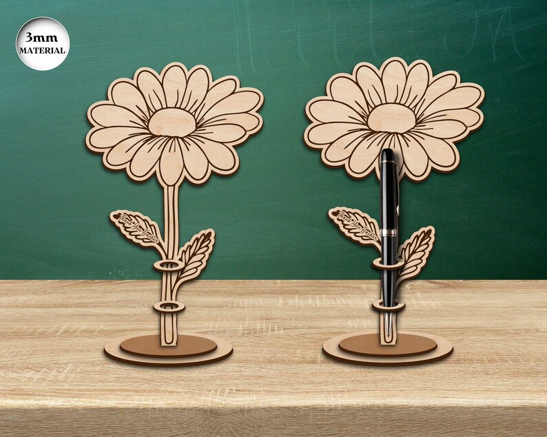 Pu&ograve; includere: Due portapenne in legno a forma di fiore, con uno spessore del materiale di 3 mm. Ogni portapenne presenta un motivo di margherita con una fessura per la penna al centro. I portapenne sono su una superficie di legno.