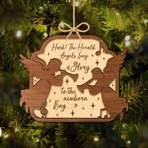 May include: Wooden Christmas ornament with a light wood center and a dark wood border. The ornament features two angel silhouettes playing trumpets, with the text "Hark! The Herald Angels Sing. Glory to the newborn King..." and star accents.