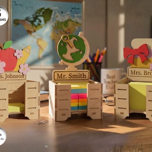 Può includere: Tre organizer da scrivania in legno con diversi design. Uno ha una mela, una matita e fiori, un altro un mappamondo e l'ultimo, libri e un fiocco. Ognuno ha un nome: Ms. Johnson, Mr. Smith e Mrs. Brown. Gli organizer sono realizzati in materiale da 3 mm.