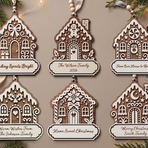 Pode incluir: Seis ornamentos de madeira em forma de casa de gengibre com detalhes brancos cortados a laser. Cada design é único, apresentando motivos como laços, boneco de gengibre, hortelã, azevinho, poinsétia ou lua, além de nomes e saudações festivas.
