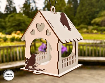 May include: A wooden bird feeder shaped like a house, with a white roof and light pink walls. The feeder has heart-shaped cutouts and a decorative bird silhouette. The text "6mm MATERIAL" is visible on the bottom left.