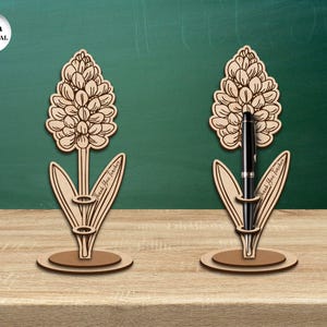 Pu&ograve; includere: Due portapenne in legno a forma di giacinto. Ogni portapenne ha una fessura per una penna e il testo "Grazie Professore" sul gambo. I portapenne sono su una superficie di legno.