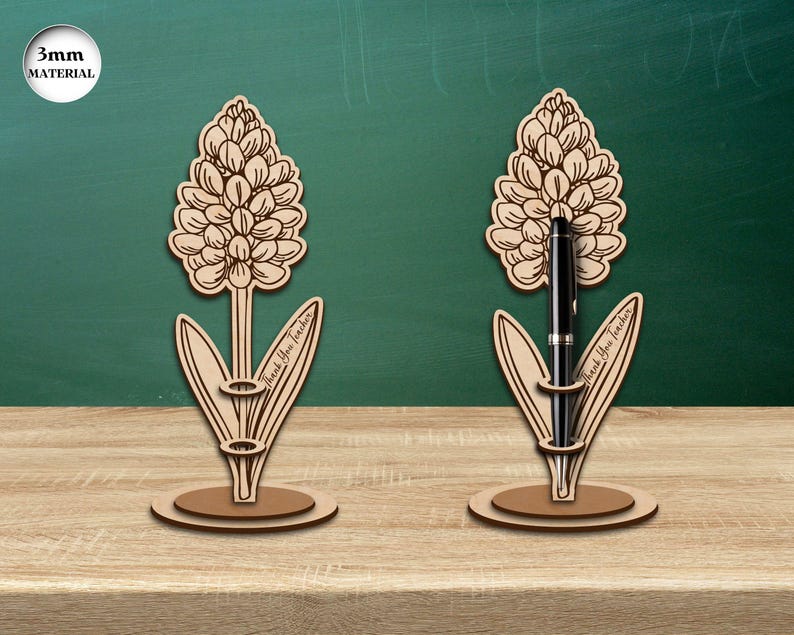 Pu&ograve; includere: Due portapenne in legno a forma di giacinto. Ogni portapenne ha una fessura per una penna e il testo "Grazie Professore" sul gambo. I portapenne sono su una superficie di legno.