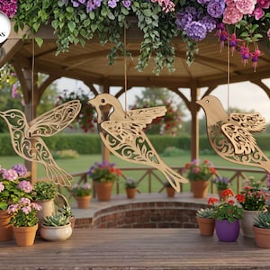 Può includere: Tre modelli di uccelli in legno con dettagli intagliati, appesi a un gazebo. Gli uccelli sono posti davanti a uno sfondo di fiori e piante in vaso. L'immagine include il testo "3 DESIGNS" in un cerchio bianco.