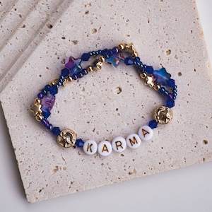 May include: A blue and gold beaded bracelet with star-shaped beads and the word "KARMA" spelled out in white beads with gold lettering.