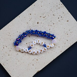 May include: A blue and white beaded bracelet with the words "It's Different" spelled out in gold letters.