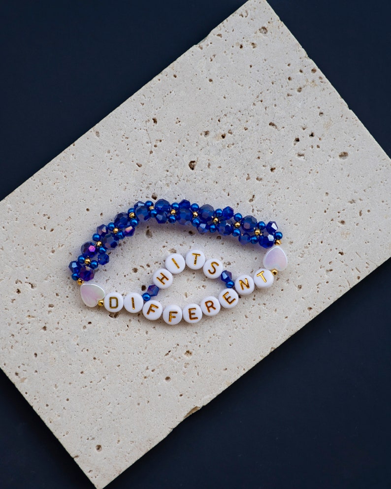 May include: A blue and white beaded bracelet with the words "It's Different" spelled out in gold letters.