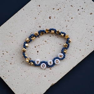 May include: A blue and gold beaded bracelet with the word "YOK" spelled out in white beads.