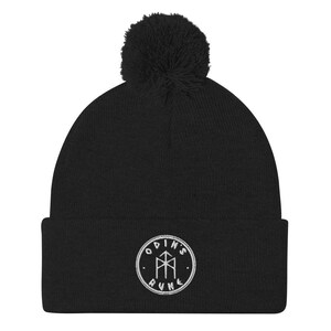 May include: Black beanie with a white pom pom and a white embroidered circle with the text "Odin's Rune" and a rune symbol inside.