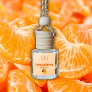 May include: A clear glass air freshener bottle with a wooden cap and a beige string for hanging. The label reads "Tangerine Dream" with a tangerine illustration. The background is a vibrant orange with tangerine slices.