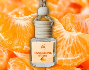 May include: A clear glass air freshener bottle with a wooden cap and a beige string for hanging. The label reads "Tangerine Dream" with a tangerine illustration. The background is a vibrant orange with tangerine slices.