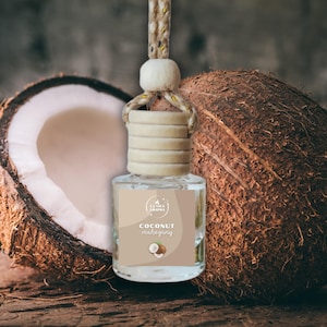 May include: A clear glass car air freshener with a wooden cap and a beige label that reads "Coconut Mahogany." The freshener hangs from a beige rope. A halved coconut and a whole coconut are in the background.