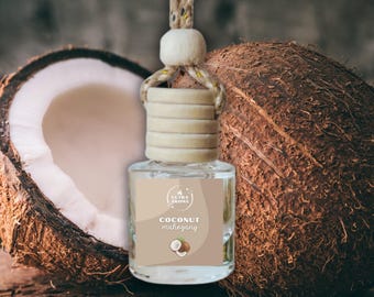 May include: A clear glass car air freshener with a wooden cap and a beige label that reads "Coconut Mahogany." The freshener hangs from a beige rope. A halved coconut and a whole coconut are in the background.