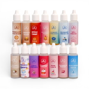 May include: A collection of twelve small, clear bottles with white caps, each labeled with a different scent name. The labels feature various colors and graphics, including images of food and flowers. Scents include Mahogany Teakwood, Apple Crisp, and Strawberry Shortcake.