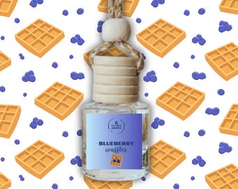 May include: A clear glass air freshener bottle with a wooden cap and a string for hanging. The label reads "Blueberry Waffles" with a waffle and blueberry graphic. The background features a pattern of waffles and blueberries.