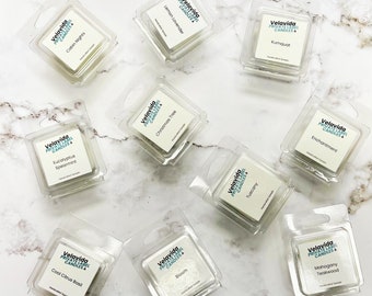 May include: Ten small, clear plastic containers with white labels. Each container holds a small, white candle. The labels have the text "Velavida Private Label Candles" and the name of the scent. The scents are Cabin Nights, Eucalyptus Spearmint, Cool Citrus Basil, Christmas Tree, Lemon Lavender, Bloom, Tuscany, Kuriquat, Enchantment, and Mahogany Teakwood.
