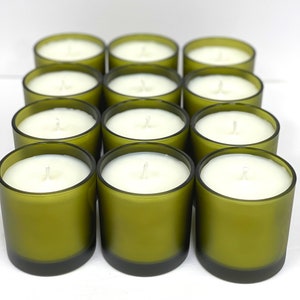 May include: A group of ten green glass candle jars with white wax and a single wick in each jar.