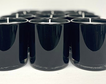 May include: A group of black glass candle jars with white wax and wicks. The jars are arranged in rows on a white surface.