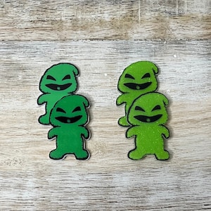 May include: Three green felt ornaments shaped like a character with a mischievous grin. The ornaments are stacked on top of each other.