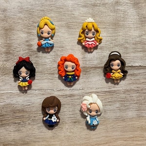 May include: Seven small, colourful, cartoon-style figurines of Disney princesses. The princesses are wearing their signature dresses and have their hair styled in their signature styles. The princesses are all facing forward and are arranged in a semi-circle.