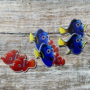 Puede incluir: Cinco adornos coloridos con forma de pez, dos peces payaso naranja y blanco y tres peces cirujano azules y amarillos. Los adornos están hechos de resina y tienen un acabado brillante.