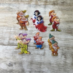 Puede incluir: Conjunto de siete figuras de personajes de Blancanieves y los Siete Enanitos. Las figuras son de madera y están pintadas en colores vivos. El conjunto incluye Blancanieves, Doc, Grumpy, Happy, Sleepy, Bashful y Sneezy.